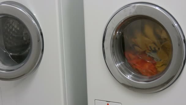 Multi-colored clothes laundry is washed in a white washing machine in the laundry room. — 비디오