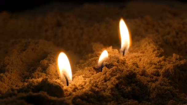 Dlouhé tenké žluté kostelní svíčky hoří v písku — Stock video