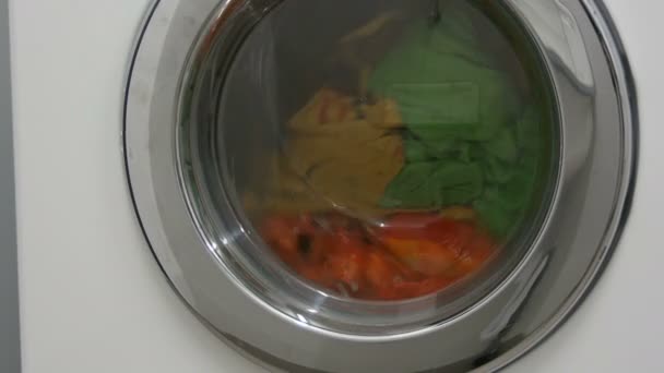 Multi-colored clothes laundry is washed in a white washing machine in the laundry room. — Stock Video