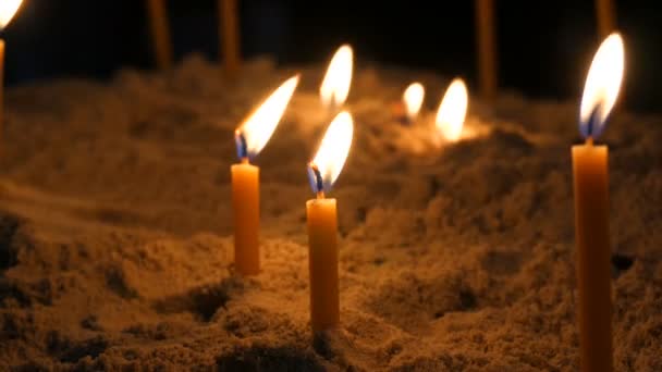 Lange dunne gele kerk kaarsen branden in het zand — Stockvideo