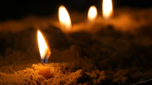 Long thin yellow church candles burn in sand — Stock Video