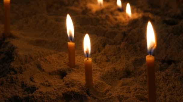 Длинные тонкие желтые церковные свечи горят в песке — стоковое видео