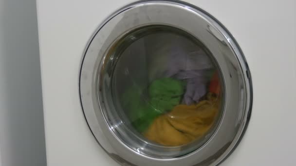 Multi-colored clothes laundry is washed in a white washing machine in the laundry room. — 비디오