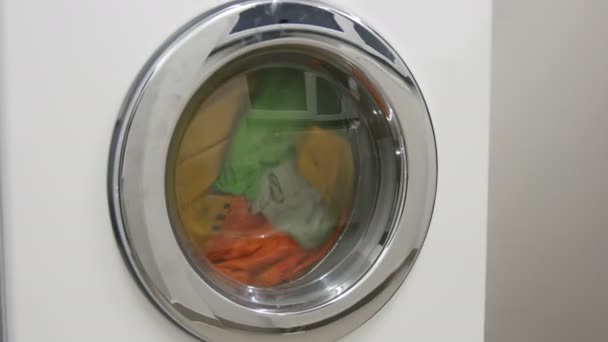 Різнокольорове прання одягу миється в білій пральній машині в пральні . — стокове відео