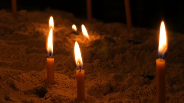 De longues bougies jaunes fines brûlent dans le sable — Video