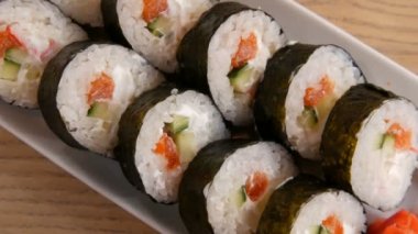 Somon, yengeç çubuğu, salatalık ve Philadelphia peynirli büyük bir suşi rulosu. Yakınlarda yeşil wasabi ve kırmızı zencefil var. Japon yemeği.
