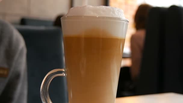 Delicioso café con leche recién hecho en una mesa en la cafetería. Espuma de leche de café con leche en un vaso especial largo transparente. El sedimento de café mezcla y hace patrones inusuales — Vídeo de stock