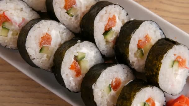 Duże bułki sushi w nori z łososiem, paluszkami krabowymi, ogórkami, serem filadelfijskim. W pobliżu jest zielony wasabi i czerwony imbir. Jedzenie japońskie — Wideo stockowe