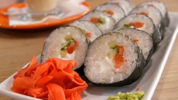 Grote sushi broodjes in een nori met zalm, krab sticks, komkommers, Philadelphia kaas. Vlakbij is groene wasabi en rode gember. Japans eten — Stockvideo
