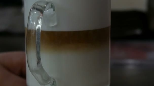 Finom frissen készített latte az asztalon a kávézóban. Tejhab tejeskávéból, átlátszó, hosszú, speciális pohárban. A kávéüledék összekeveri és szokatlan mintákat készít. — Stock videók