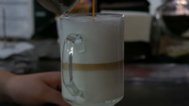 Café con leche en un vaso largo transparente. Barista hace un café con leche, vertiendo una fina corriente de café en la leche — Vídeos de Stock