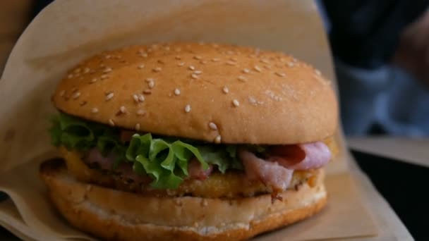 Deliciosa hamburguesa fresca jugosa en la mesa en el restaurante de comida rápida. Hojas de ensalada, bollo fresco, chuleta de carne, salsa malsana — Vídeos de Stock