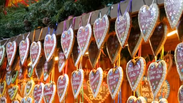 Hermosas deliciosas galletas de jengibre de Navidad en forma de corazón cuelgan en un mostrador de quiosco. Mercado tradicional europeo de Navidad. Inscripción en alemán — Vídeos de Stock