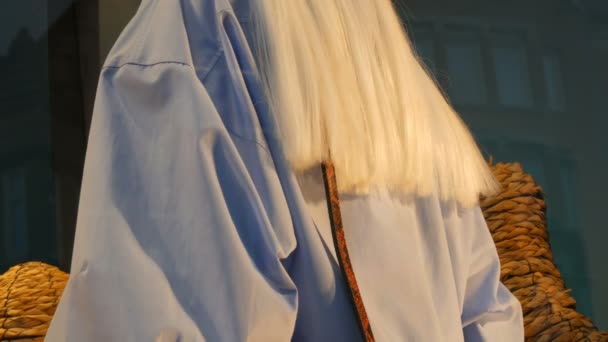 Часть женского манекена с белым длинным слухом. Манекен в витрине. На витрине бутика представлена дорогая, модная одежда — стоковое видео