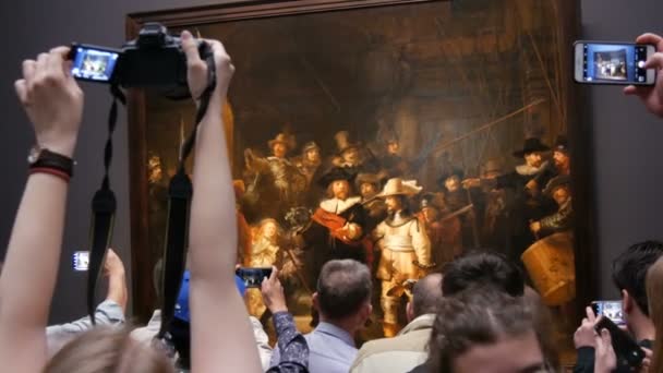 АМСТЕРДАМ, НИДЕРЛАНДЫ - 25 апреля 2019 года: Люди фотографируют на мобильный телефон и смотрят фильм "Ночной дозор Рембрандта" в Рейксмусеуме. Толпа туристов, интересующихся искусством . — стоковое видео