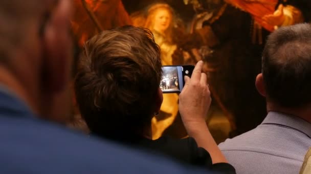 Amsterdam, 25 april 2019: Mensen maken foto 's op de mobiele telefoon en bekijken foto' s De Nachtwacht van Rembrandt, in het Rijksmuseum. Publieke toerist geïnteresseerd in kunst. — Stockvideo