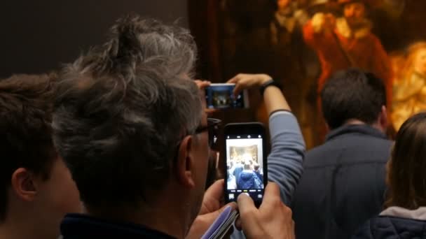 AMSTERDAM, NETHERLANDS - 25 April, 2019: People take pictures on the mobile phone and watching picture The Night Watch of Rembrandt, in Rijksmuseum. Crowd tourist interested in art. — Stock Video