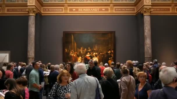 AMSTERDAM, PAÍSES BAJOS - 25 de abril de 2019: Gente viendo la foto La Guardia Nocturna de Rembrandt, en el Rijksmuseum. Multitud de turistas interesados en el arte . — Vídeos de Stock
