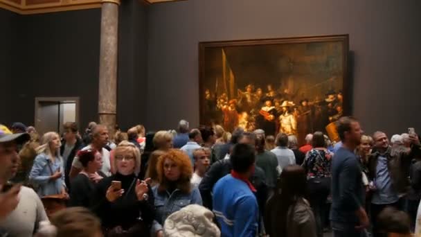 AMSTERDAM, PAÍSES BAJOS - 25 de abril de 2019: Gente viendo la foto La Guardia Nocturna de Rembrandt, en el Rijksmuseum. Multitud de turistas interesados en el arte . — Vídeos de Stock