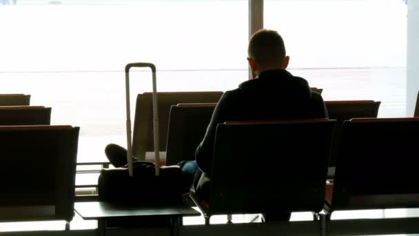 Silhueta de um homem com mala esperando no aeroporto antes da partida — Vídeo de Stock