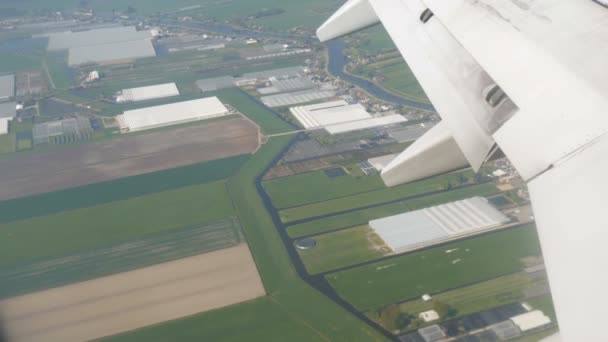 Het vliegtuig bereidt zich voor op de landing. Vliegen over water kanalen, kassen, boerderijen met zonnepanelen, huizen, de route van de stad Amsterdam, Nederland, Nederland — Stockvideo