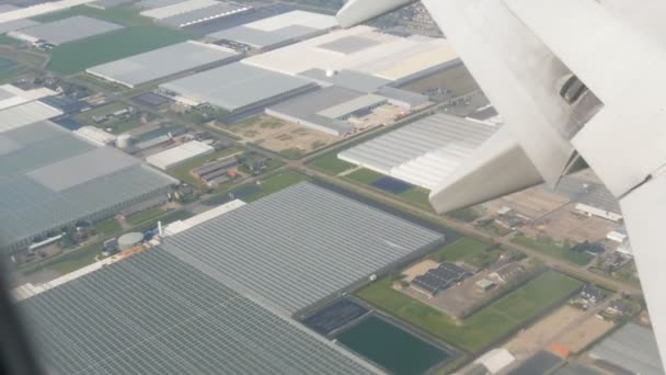 Samolot przygotowuje się do lądowania. Latanie nad kanałami wodnymi, szklarnie, farmy z panelami słonecznymi, domy, droga miasta Amsterdam, Holandia, Niderlandy — Wideo stockowe