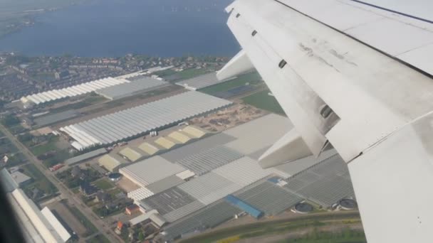 O avião está a preparar-se para aterrar. Voando sobre canais de água, estufas, fazendas com painéis solares, casas, a rota da cidade de Amsterdã, Holanda, Países Baixos — Vídeo de Stock