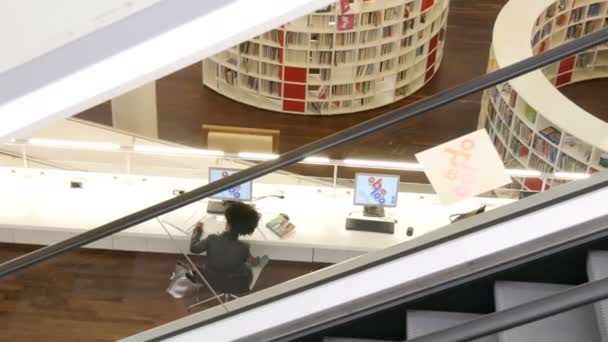 Amsterdam, Niederlande - 24. April 2019: modernes neues Regal mit Bücherregalen mit verschiedenen Büchern in der öffentlichen Bibliothek, das Mädchen lernt am Tisch — Stockvideo
