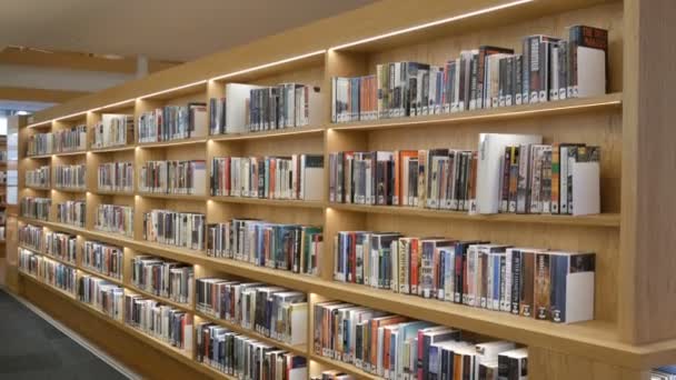 Amszterdam, Hollandia - 2019. április 24.: Modern, új polcok könyvespolcokkal, különböző könyvekkel a közkönyvtárban — Stock videók