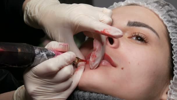 Tatuaje de labio Microblading con un pigmento rojo colorante especial que corrige el color de los labios en una clínica de cosmetología. Procedimiento permanente de los labios del maquillaje que aplica el maquillaje del pigmento en labios con una máquina del tatuaje — Vídeo de stock