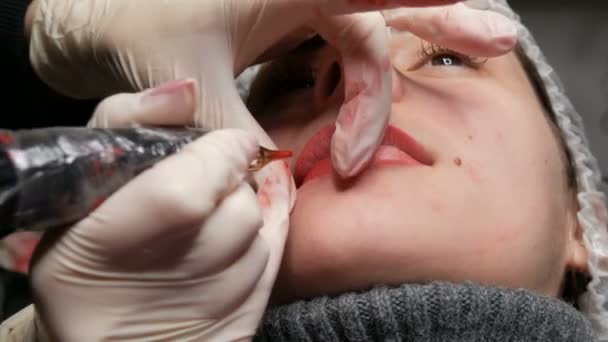 Microblading lip tattoo met een speciale kleuring rood pigment dat lipkleur corrigeert in een cosmetische kliniek. Permanente make-up lippen procedure aanbrengen pigment make-up op de lippen met een tattoo machine — Stockvideo