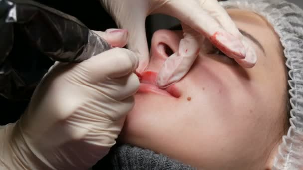 Permanent makeup läppar förfarande. Händerna i latexhandskar från en skicklig kosmetolog som applicerar pigmentmakeup på läpparna med en tatueringsmaskin. Mikroblades, mikropigmentering läppar arbete — Stockvideo