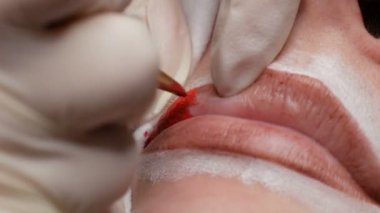 Kalıcı makyaj dudakları prosedürü. Elleri lateks eldivenli yetenekli bir kozmetik uzmanının dudaklarına dövme makinesiyle pigment makyaj uygulaması. Mikroplanma, mikro pigmentasyon dudaklar çalışıyor. Makro çekim.