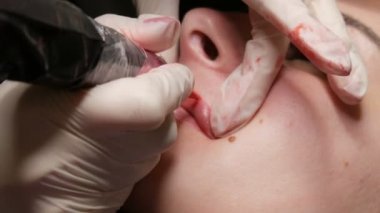 Kalıcı makyaj dudakları prosedürü. Elleri lateks eldivenli yetenekli bir kozmetik uzmanının dudaklarına dövme makinesiyle pigment makyaj uygulaması. Mikroplanma, mikro pigmentasyon dudaklar çalışıyor.