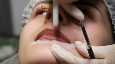 Mikroplu patinaj, mikro pigmentasyon dudaklar güzellik salonunda çalışır. Dudakları çizilmiş ve kalemle boyanmış bir kadın, yarı kalıcı makyaja hazırlanıyor.