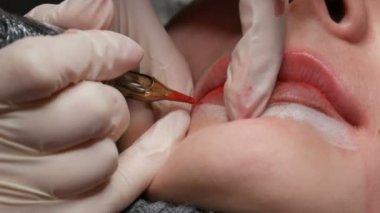 Mikro patenli dudak dövmesi ve kozmetoloji kliniğindeki dudak rengini düzelten kırmızı pigment. Kalıcı makyaj dudakları prosedürü. Dövme makinesiyle dudaklara pigment makyaj uygulanıyor.