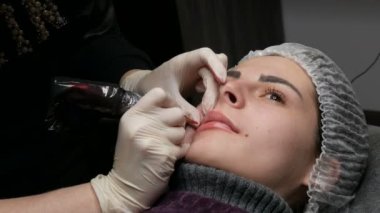 Mikro patenli dudak dövmesi ve kozmetoloji kliniğindeki dudak rengini düzelten kırmızı pigment. Kalıcı makyaj dudakları prosedürü. Dövme makinesiyle dudaklara pigment makyaj uygulanıyor.