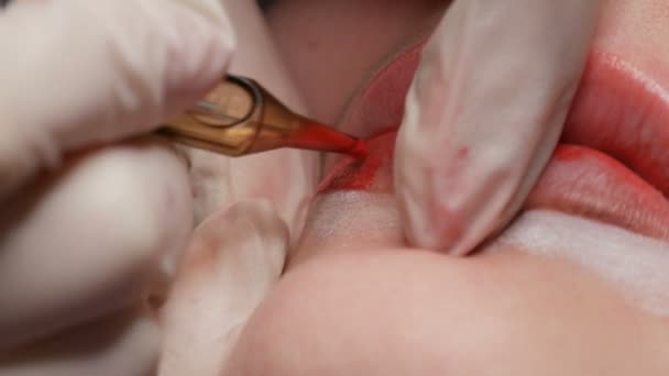 Microblading τατουάζ χειλιών με ένα ειδικό χρωματισμό κόκκινη χρωστική ουσία που διορθώνει το χρώμα των χειλιών σε μια κλινική κοσμετολογίας. Μόνιμη διαδικασία μακιγιάζ χείλη εφαρμογή χρωστική μακιγιάζ στα χείλη με ένα μηχάνημα τατουάζ κοντά — Αρχείο Βίντεο