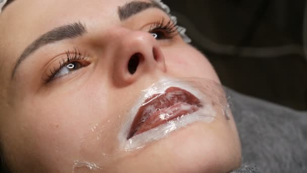 A kozmetikus mester speciális érzéstelenítést alkalmaz az ajkakon. Készülődés az állandó ajaksminkre. Modern arc tetoválás — Stock videók