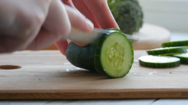 Bıçakla kesilmiş kadın elleri mutfak tahtasında taze yeşil bir salatalık. Sağlıklı vejetaryen yemekleri