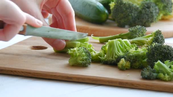 Weibliche Hände schneiden mit einem Messer frischen grünen Brokkoli auf einem Küchentisch. Gemüse mit einem Messer in Stücke schneiden. Veganes Essen. — Stockvideo