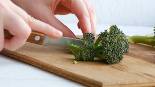 여자 손은 신선 한 녹색 브로콜리 양배추를 우묵 하게 썰어서 식탁에 올려 놓는다. 칼로 야채를 썰어 요리하라. 채식 식품. — 비디오
