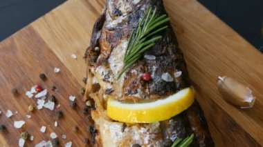 Bir dilim limonla doldurulmuş ve biberiye tütsülenmiş uskumru filizi ile süslenmiş kiraz domatesleri, sarımsak, kaba tuz ve biber ve zeytinyağı yanında ahşap bir doğrama tahtasının üzerinde