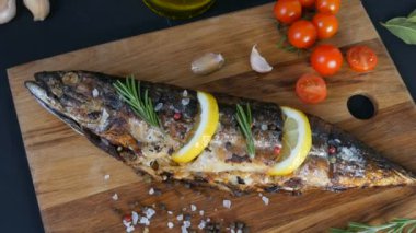 Lezzetli taze balık, ahşap bir tahtanın üzerinde füme uskumru, kiraz domateslerinin yanında, sarımsak, kaba tuz ve biber, limon dilimleri ve yeşil biberiye ile süslenmiş.