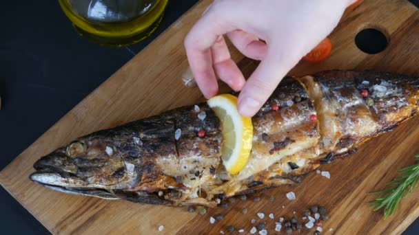 Ruce nadívané plátkem citronu a zdobené krajkou rozmarýnu uzené makrely na dřevěné sekané desce vedle cherry rajčat, česneku, hrubé soli a pepře a olivového oleje — Stock video