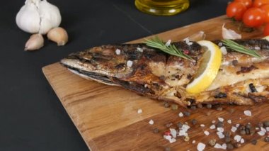 Lezzetli taze balık, ahşap bir tahtanın üzerinde füme uskumru, kiraz domateslerinin yanında, sarımsak, kaba tuz ve biber, limon dilimleri ve yeşil biberiye ve zeytinyağı ile süslenmiş.