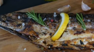 Bir dilim limonla doldurulmuş ve biberiye tütsülenmiş uskumru filizi ile süslenmiş kiraz domatesleri, sarımsak, kaba tuz ve biber ve zeytinyağı yanında ahşap bir doğrama tahtasının üzerinde