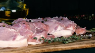 Ahşap mutfak tahtasının üzerinde domuz pastırması taze dilimler. Sarımsak, biberiye dalı, kaba tuz, biber, zeytinyağı. Ev yapımı yemek..