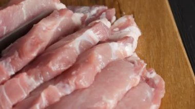 Bir aşçının kadın ellerine yakından bak. Büyük bir mutfak bıçağıyla ahşap mutfak tahtasına domuz pastırması dilimleri kes.