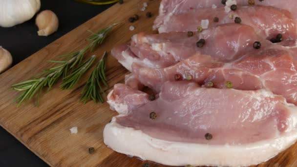 Pedaço de carne de porco bacon rosa grande fresco em uma tábua de corte de cozinha caseira em um estilo rústico decorado com pimenta preta e vermelha e sal grosso — Vídeo de Stock